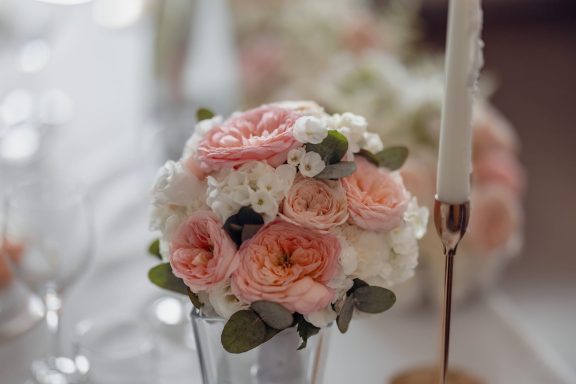 Vase mit rosa und weißen Blumen, umgeben von Gläsern und einer Kerze.