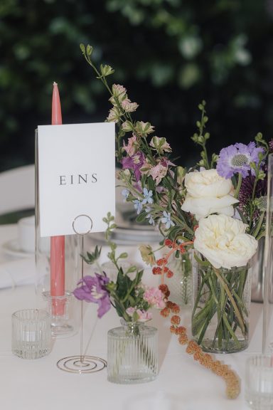 Tischdekoration mit bunten Blumen in Vasen und einer Speisekarte.