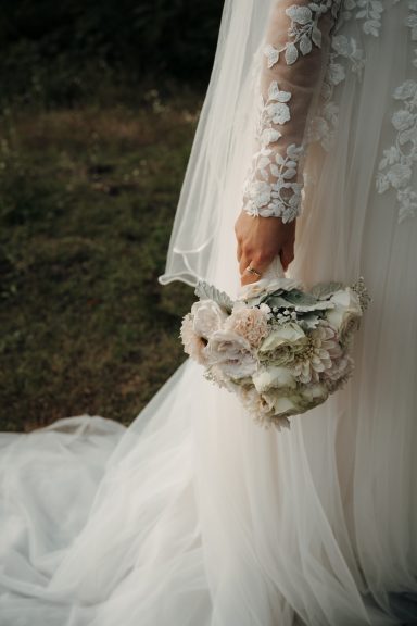 Braut hält einen Blumenstrauß aus zarten, pastellfarbenen Blumen.