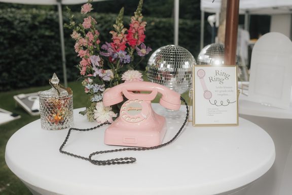 Rosa Telefon auf einem Tisch, umgeben von Blumen und einer dekorativen Glasvase.