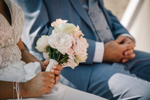 Braut hält einen bunten Blumenstrauß, während der Bräutigam daneben sitzt.