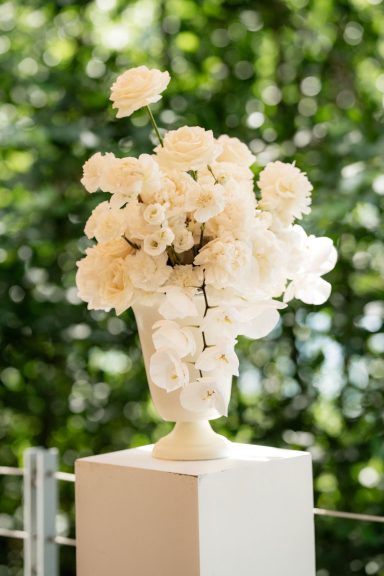 Weißer Blumenstrauß in einer eleganten Vase vor grünem Hintergrund.