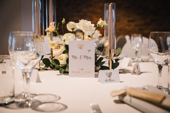 Tischdekoration mit Blumen, Gläsern und Platzkarten für eine elegante Veranstaltung.