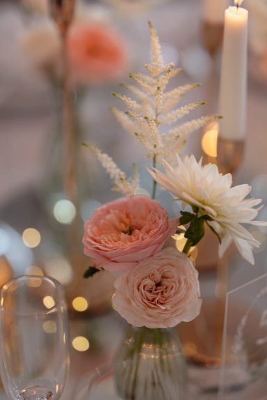 Ein Bouquet aus Pastellblumen in einer Glasvase, umgeben von Kerzenlicht.