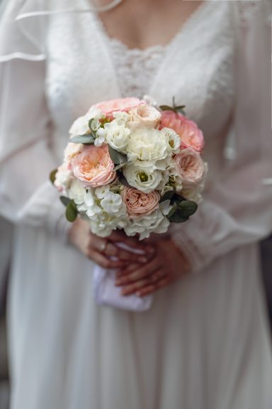 Hochzeitsstrauß mit rosa und weißen Blumen, gehalten von einer Person in einem Brautkleid.
